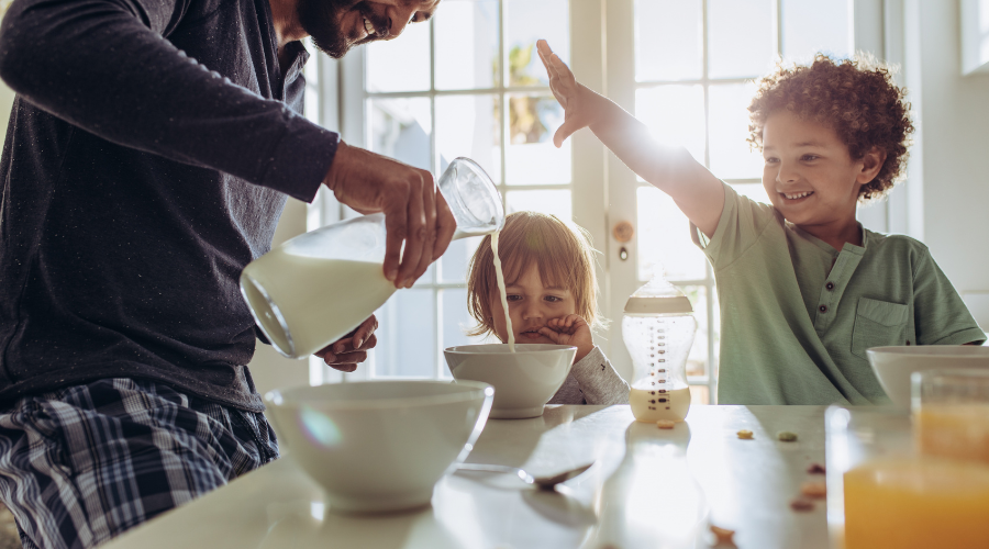 　朝の食卓で父親がボウルに牛乳を注ぐ様子を幼い子ふたりが見ている